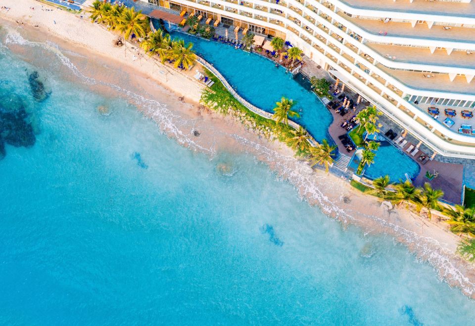 aerial view of a beautiful beach resort with a large pool surrounded by palm trees , chairs , and umbrellas at Seashells Phu Quoc Hotel & Spa