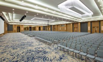 a large , empty conference room with rows of chairs and a carpeted floor , under a high ceiling with recessed lights at Rixos Water World Aktau