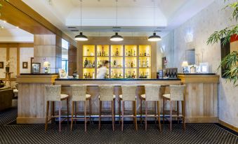 a modern bar with wooden tables , white stools , and a variety of bottles behind the counter at Riviera Hotel