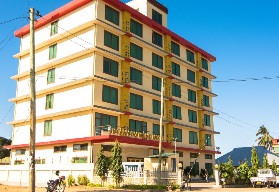 a tall building with a red and yellow facade is situated on a street corner at Tiffany Diamond Hotels - Mtwara