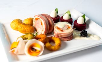 a white plate filled with a variety of appetizers , including meat , cheese , and fruit , arranged on a dining table at Grand Hotel