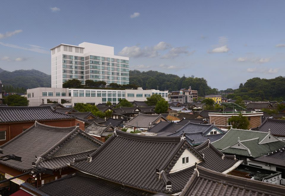 a traditional asian village with a large white building in the background , surrounded by green trees and blue skies at Lahan Hotel Jeonju