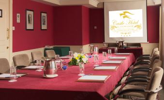 a long dining table with red tablecloths , set for a meeting , and a projector screen displaying a movie logo at Castle Hotel Macroom