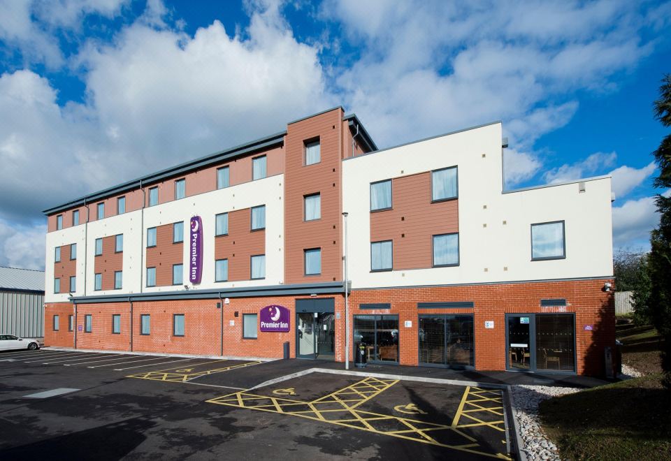 a modern hotel building with a large glass window and a parking lot in front of it at Premier Inn Honiton