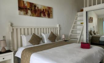 a white bedroom with a double bed and a bunk bed , as well as a staircase leading to a loft area at The Beachhouse