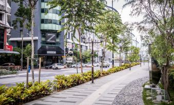 a paved walkway surrounded by trees and bushes , with a sidewalk on the right side at Z Hotel