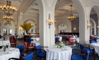 a luxurious dining room with white walls , blue tables , and chairs , and a chandelier hanging from the ceiling at The Phoenicia Malta