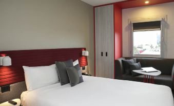 a modern hotel room with a large bed , white linens , and a view of the city through a window at Ibis Sydney Airport