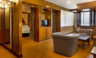 a spacious living room with hardwood floors , a couch , a chair , and a television . also a dining table in the room at Phrae Nakara Hotel