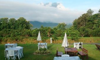 a grassy field with several tables and chairs set up for outdoor dining , surrounded by trees and mountains in the background at Aurora Resort Chiangdao
