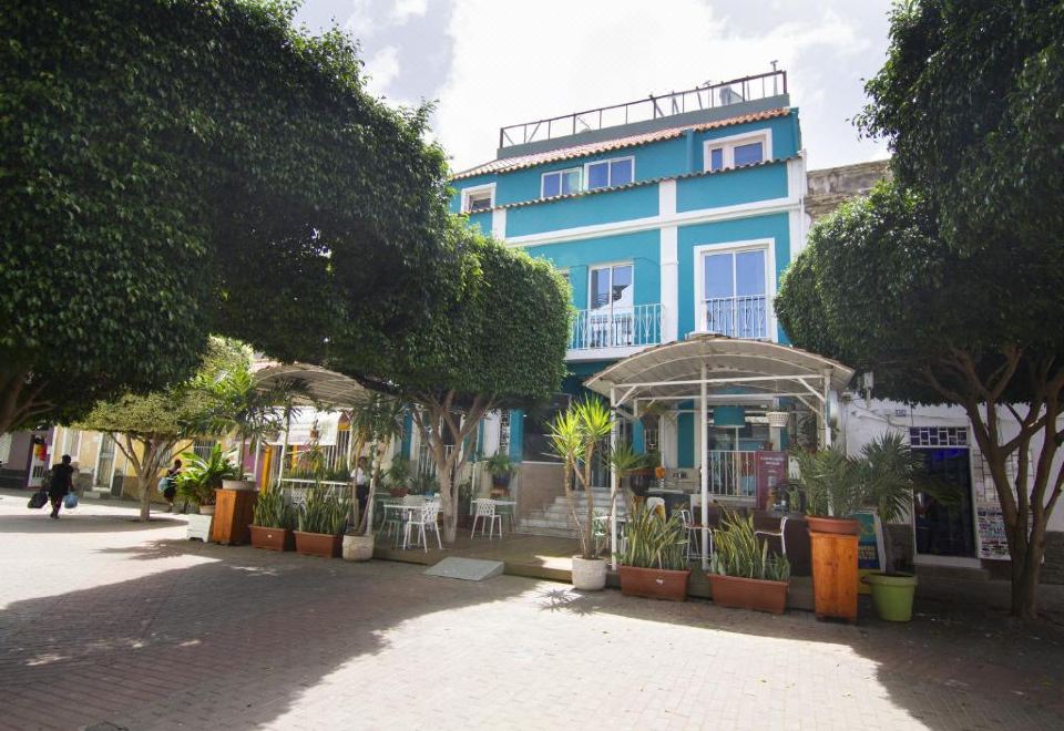 a blue building with a white balcony and palm trees , surrounded by potted plants and umbrellas at Hotel Santa Maria