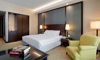 A bedroom is furnished with a large bed, a white chair in the middle, and a side table at Eastin Hotel Kuala Lumpur