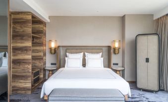 a large bed with white linens and a headboard is situated in a room with wooden walls and lamps at Swissôtel Jakarta Pik Avenue