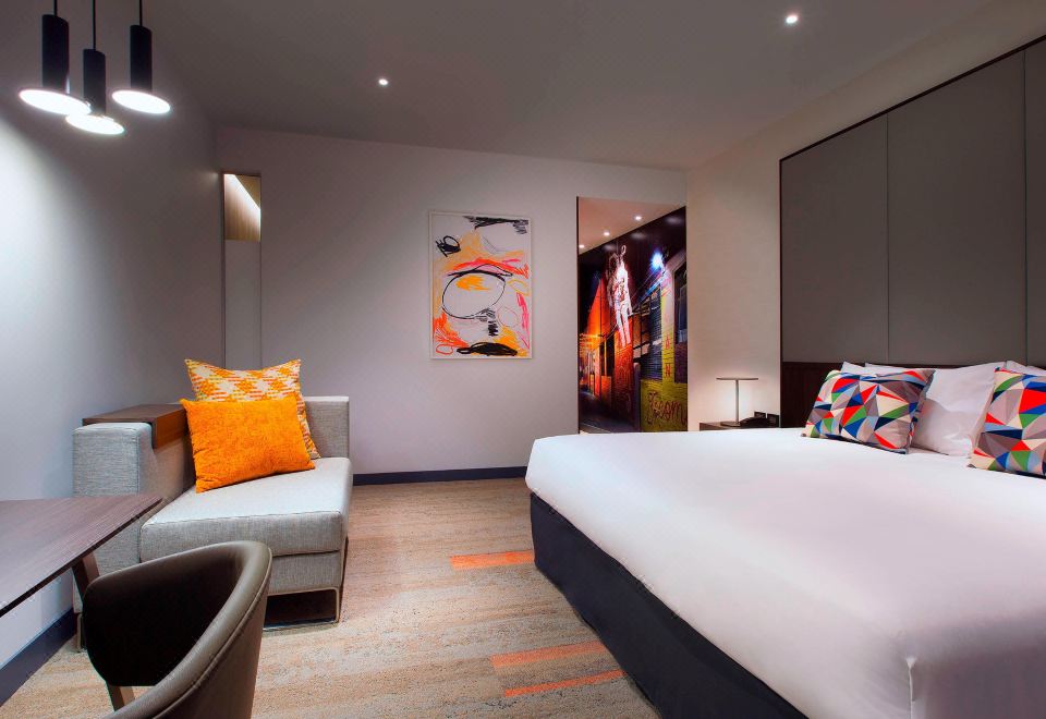 a modern hotel room with a white bed , orange pillows , and a colorful abstract painting on the wall at Aloft Perth