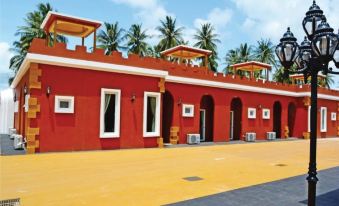 a red building with yellow walls and a yellow gate in front of it , surrounded by palm trees at World Cat Hotel Beach & Resort