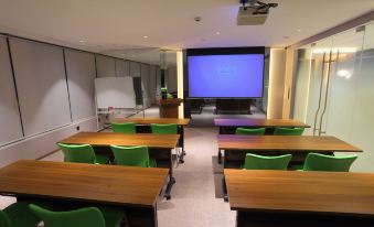 a classroom with green chairs and desks , a whiteboard , and a large screen on the wall at Ibis Styles Hotel