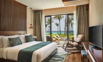 a modern bedroom with a large window offering a view of the ocean , featuring white bedding , wooden furniture , and a comfortable seating area at Movenpick Resort Cam Ranh