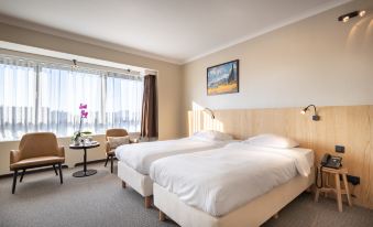 a hotel room with two beds , a window , and a table , all decorated in white at Hotel Carlton