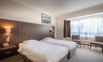 a hotel room with two beds , a window , and a chair , all neatly made up at Hotel Carlton