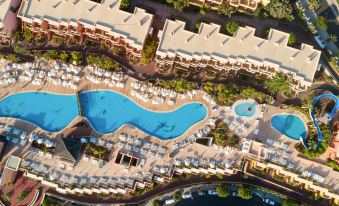 aerial view of a resort with a large pool surrounded by buildings , and numerous chairs and umbrellas placed around the pool area at Landmar Costa Los Gigantes