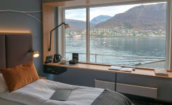 a bedroom with a large window overlooking a body of water , featuring a bed and a desk at Scandic Ishavshotel