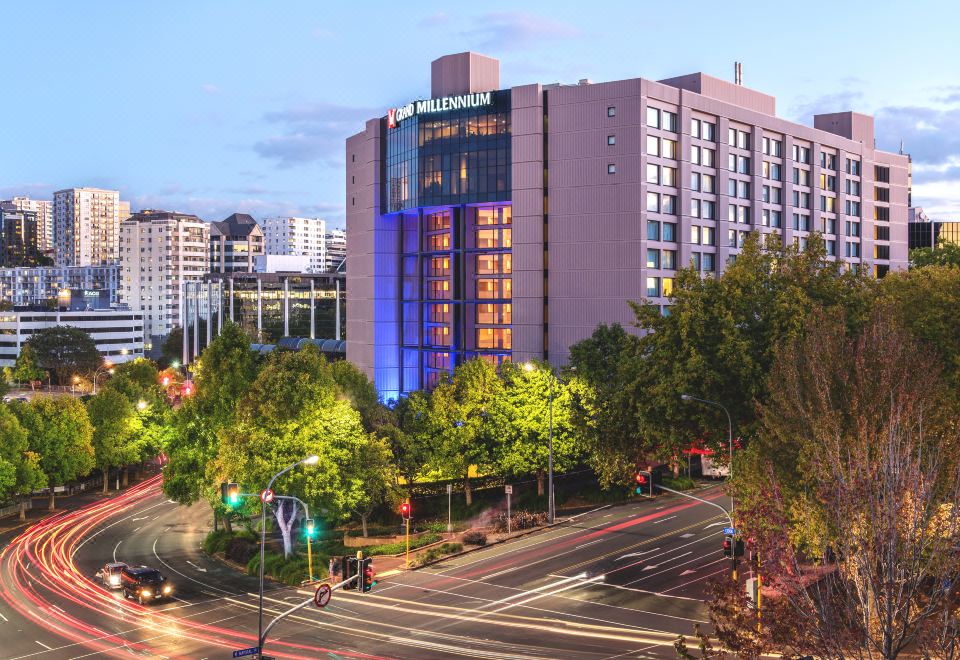 a large hotel with a blue and purple facade is surrounded by trees and traffic at Grand Millennium Auckland