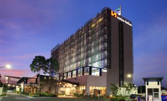 a tall building with a large glass facade and the hilton hotel logo lit up at night at Swiss-Belinn Modern Cikande