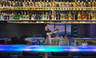 A woman stands behind the bar of an upscale restaurant, where bottles and glasses are on display at Kasion K Hotel Yiwu