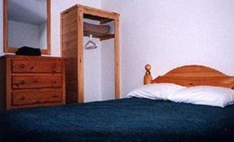 a cozy bedroom with a blue bedspread , wooden furniture , and a hanging coat rack on the wall at Chisholms of Troy Coastal Cottages