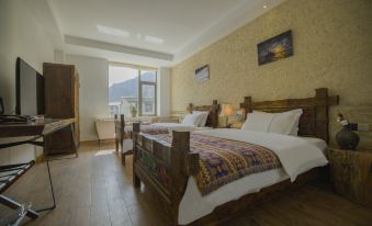 In the room, there is a bed with two windows and a wooden headboard, as well as a side table at Hotel Blanche Yading