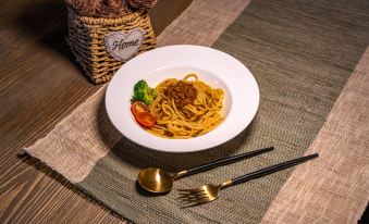 a white plate filled with spaghetti and meat sauce sits on a dining table , accompanied by a fork , spoon , and knife at Amble Hotel