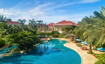 a large swimming pool surrounded by lush greenery , with several lounge chairs and umbrellas placed around it at Dheva Mantra Resort