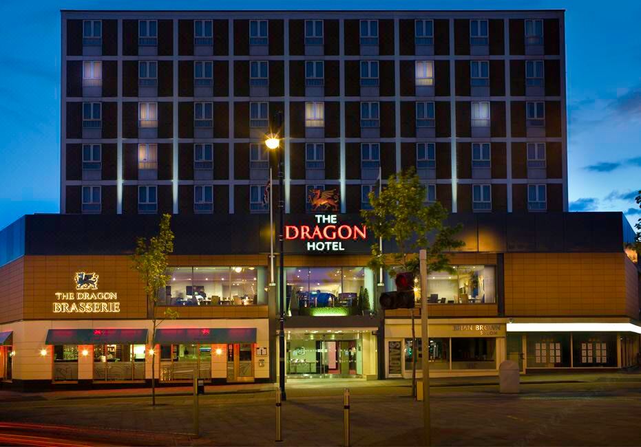 a hotel at night , with a large building in the foreground and people walking around at The Dragon Hotel