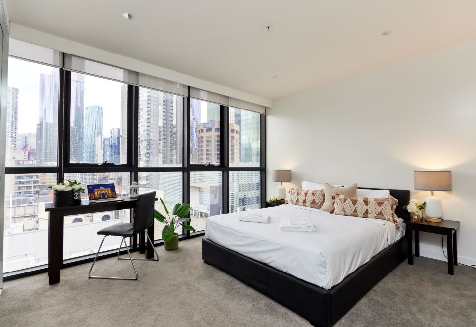 a modern bedroom with a large window overlooking the city , a black bed , and a desk at Arrow on Swanston