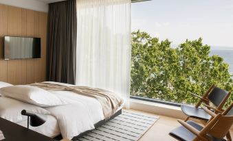 a modern bedroom with a large window offering a view of the outdoors , featuring a bed , nightstand , and rug at Briig Boutique Hotel