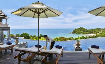 a woman is preparing her sunbed on a deck overlooking the ocean , with a view of the water in the distance at Pimalai Resort & Spa