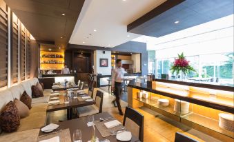 a modern restaurant with a chef preparing food in the kitchen , and a dining area filled with tables and chairs at Kantary Hotel Kabinburi