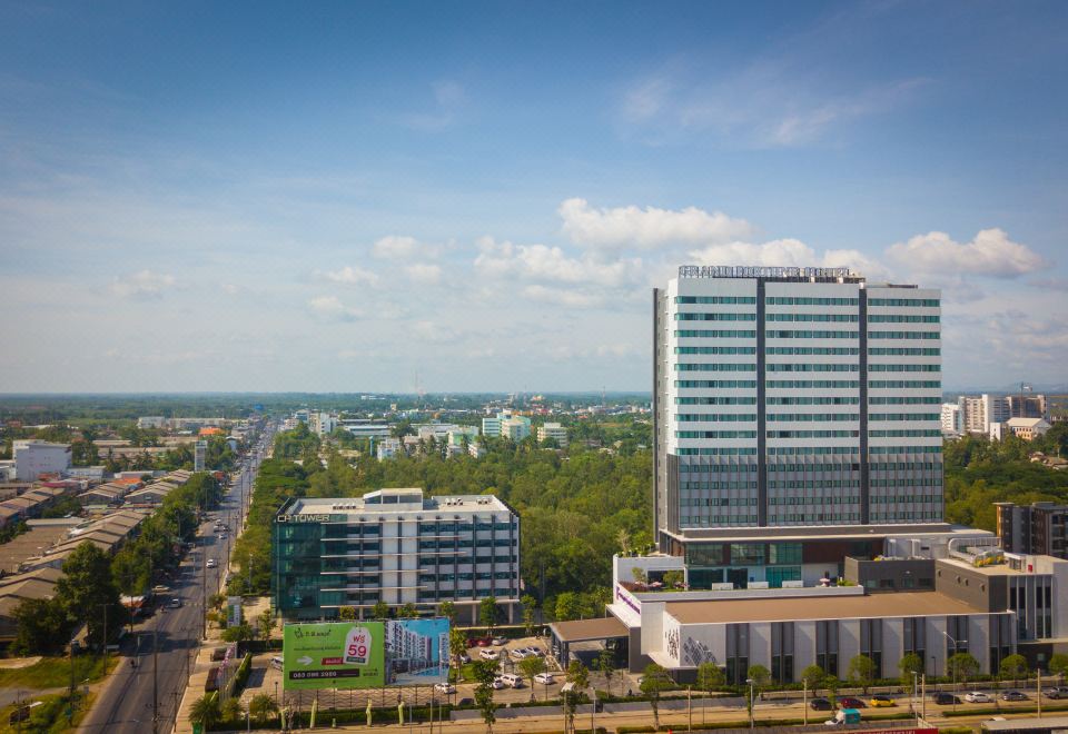 a cityscape with a tall building in the foreground and a car driving on a road at Grand Fortune Hotel Nakhon Si Thammarat