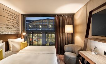 a hotel room with a large bed , a chair , and a view of the city at HYPERION Hotel Leipzig