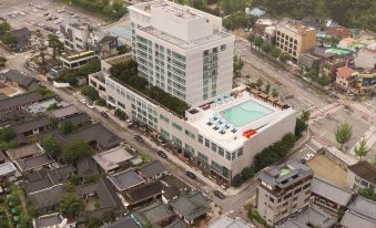 a large white building with a pool and trees in the background , surrounded by other buildings and streets at Lahan Hotel Jeonju