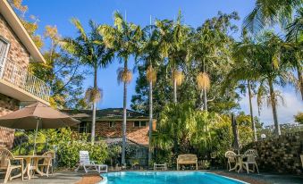 a large swimming pool surrounded by palm trees and chairs , with a house in the background at Econo Lodge Lilydale