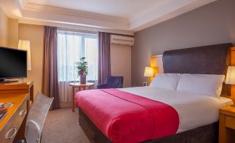 a large bed with a red blanket is in the middle of a room with a window , desk , and chair at The Prince of Wales Hotel