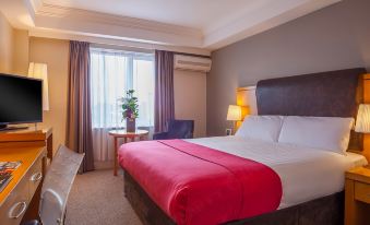 a hotel room with a red bed , white sheets , and a red blanket , along with a desk and chair at The Prince of Wales Hotel