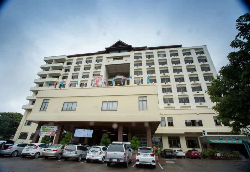 a large , white building with a green roof and many cars parked in front of it at Phrae Nakara Hotel