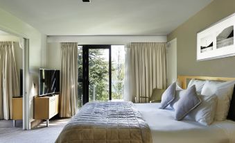 a spacious bedroom with a king - sized bed , a flat - screen tv , and a large window overlooking the outdoors at Novotel Queenstown Lakeside