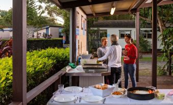 a group of people standing around a dining table in a backyard , enjoying a meal together at Discovery Parks - Emerald Beach
