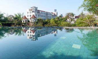 a large outdoor swimming pool surrounded by buildings , with a reflection of the building in the water at El Hotel Malang