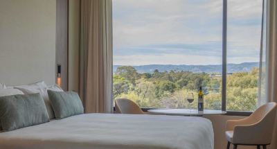 a hotel room with a large window overlooking a beautiful view of the mountains , and a bed with white sheets at Oval Hotel at Adelaide Oval, an EVT hotel