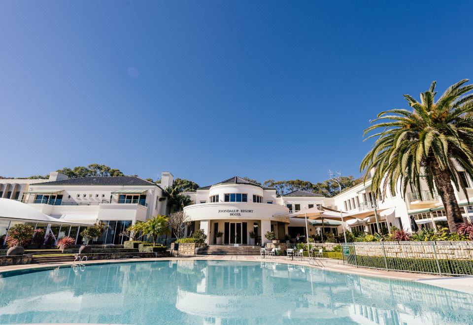 a large white building with a pool in front of it , surrounded by palm trees at Joondalup Resort