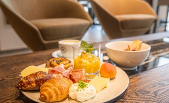 a dining table with a plate of breakfast food , including croissants , ham , and a glass of juice at Maseven Muenchen Messe Dornach